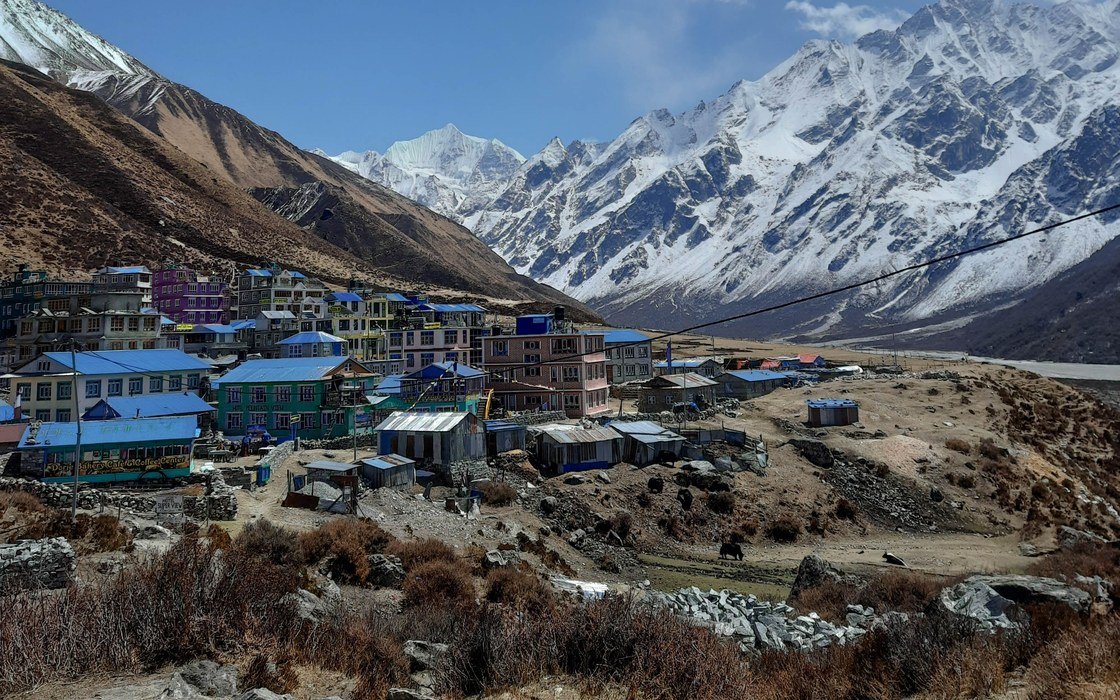 A village of low buildings below snow covered peaks in the Langtang valley in Nepal