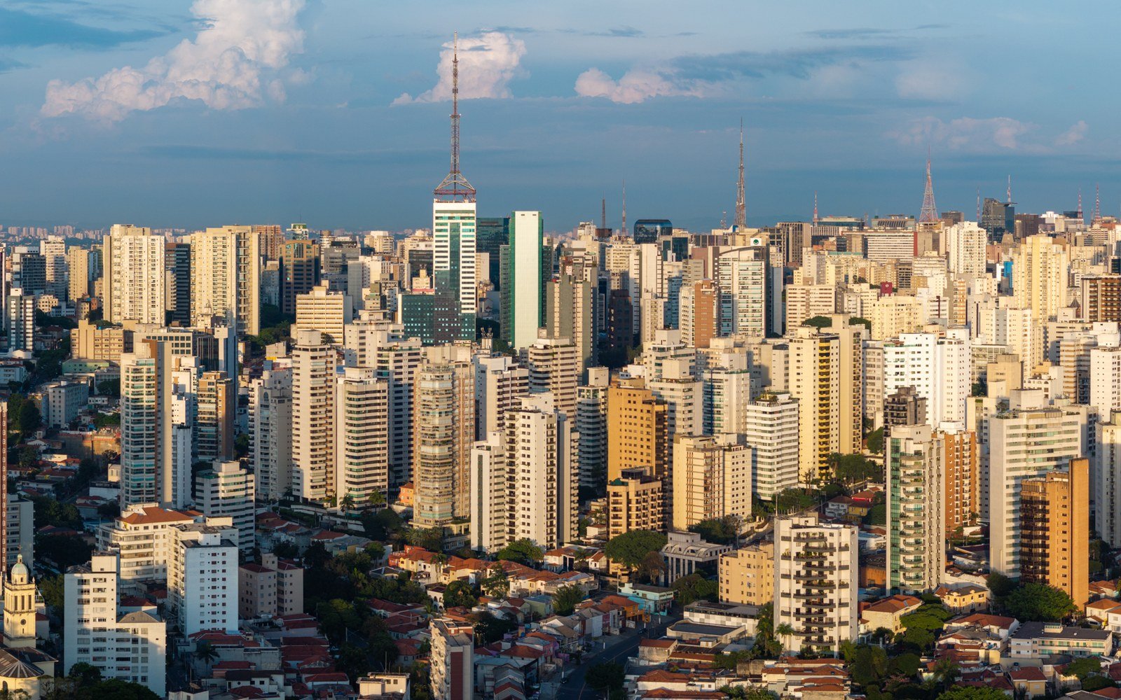 An aerial view across the dense high rise skyline of Sao Paulo in daylight, towers stretching to the horizon under scattered cloud