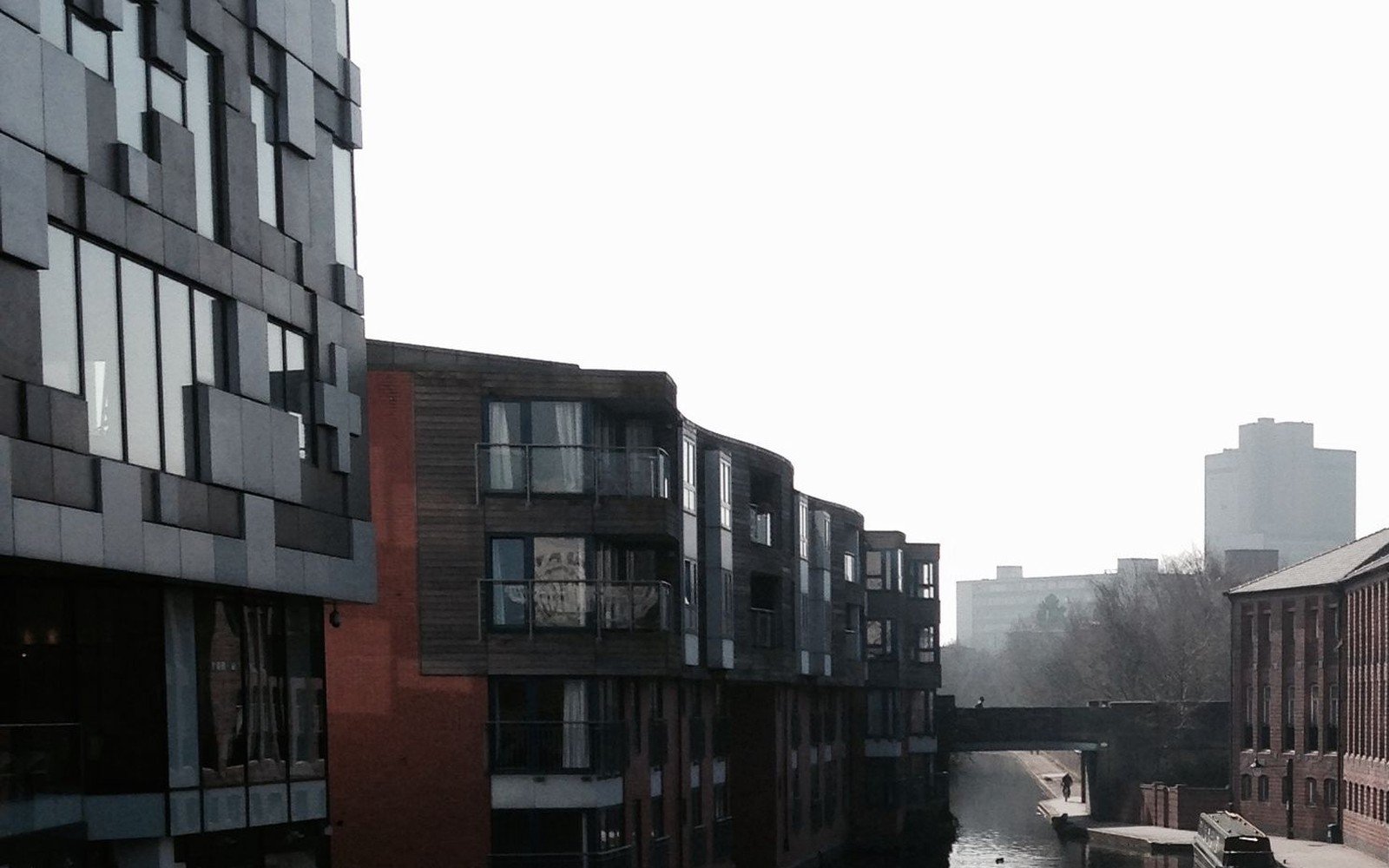 Modern canal side apartment blocks and an older brick warehouse beside still water in England