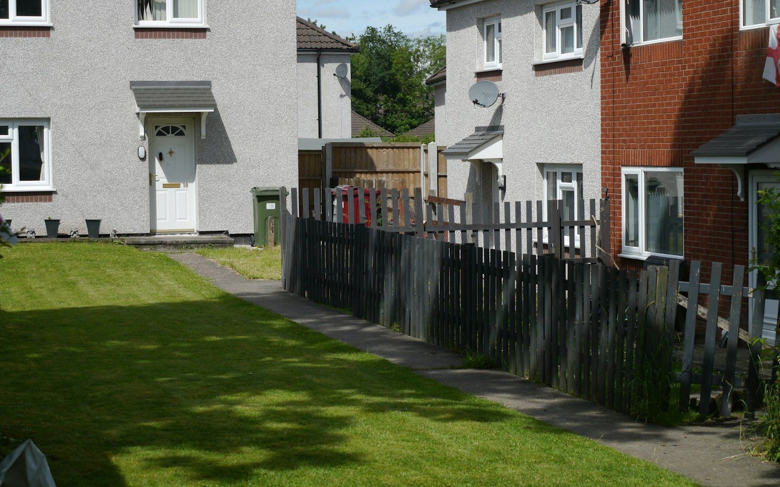 A pair of rendered and brick semi-detached houses behind a mown front lawn and a low timber fence