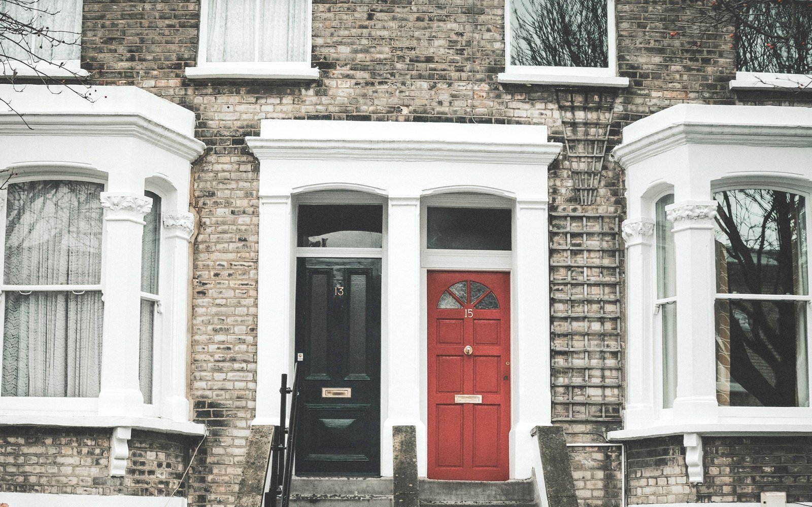 The front doors of two adjoining town houses in a terrace, one painted black and one painted red, with white rendered surrounds and bay windows either side