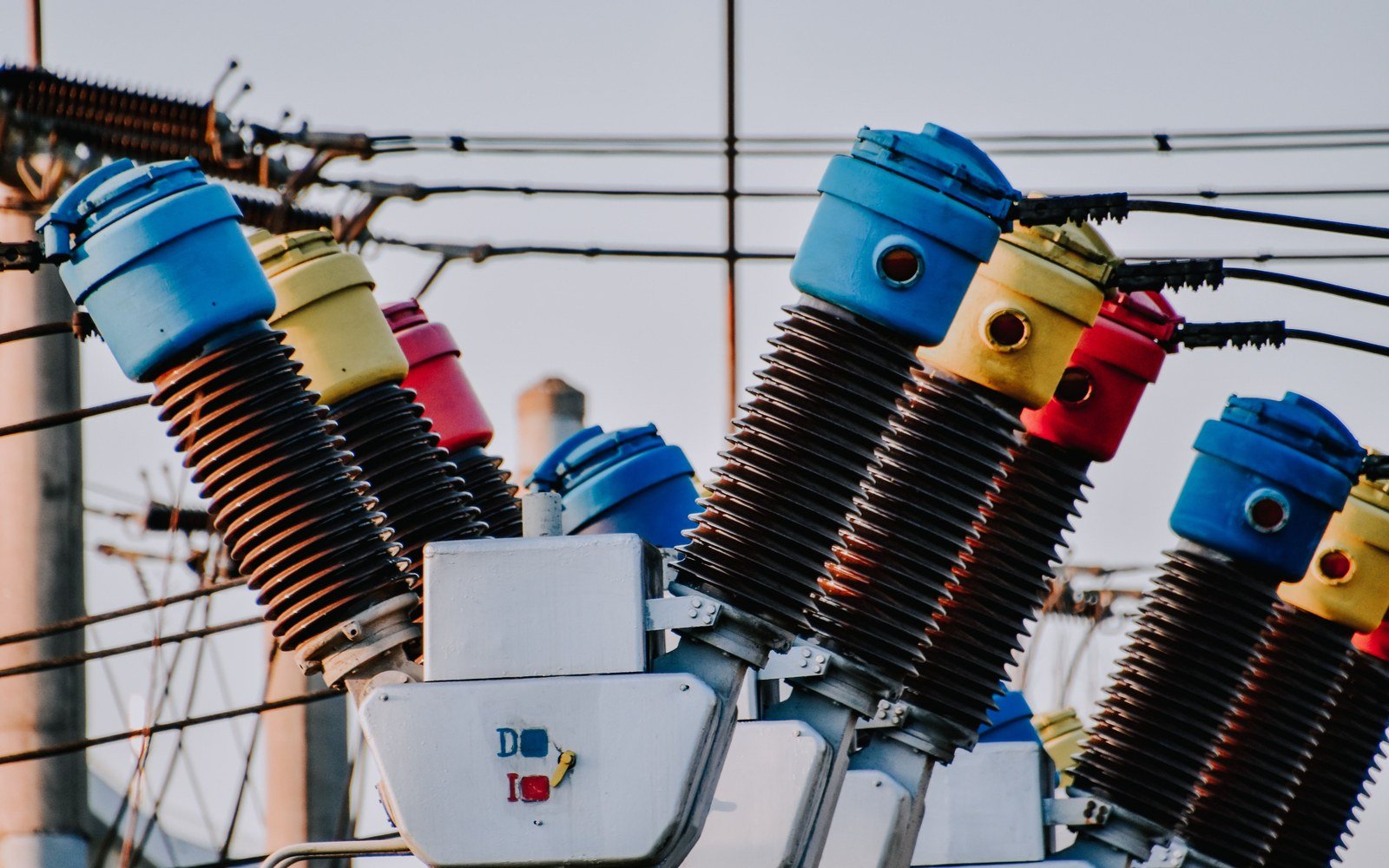 A row of high voltage switchgear insulators with coloured caps, ribbed brown stacks carrying conductors away on both sides