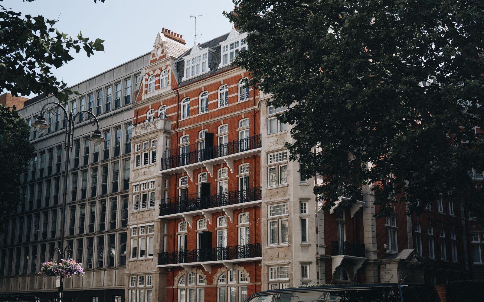 A red brick residential block of several storeys with stone dressings and tall sash windows, seen from the street on a bright day