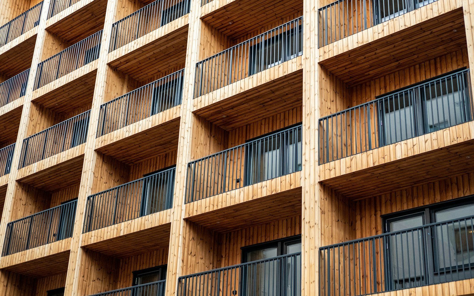 The face of a modern apartment block with recessed balconies lined in timber boarding and dark metal balustrades