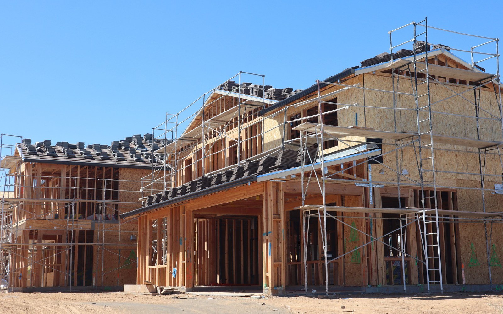 A timber framed house under construction behind scaffolding, with roof tiles stacked on the battens