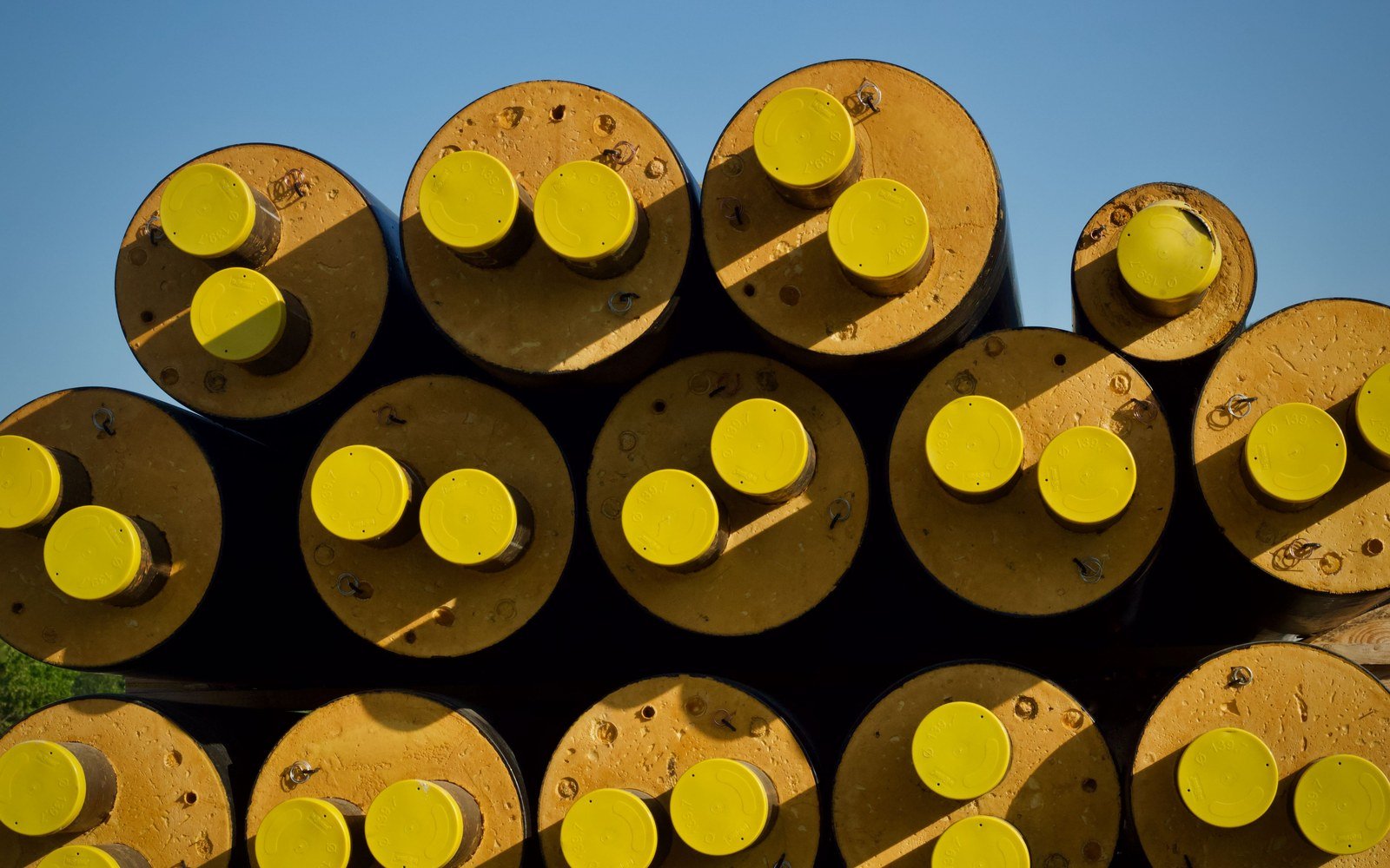 Stacked large diameter steel pipe seen end on, each bore closed with a yellow protective cap, against a clear sky