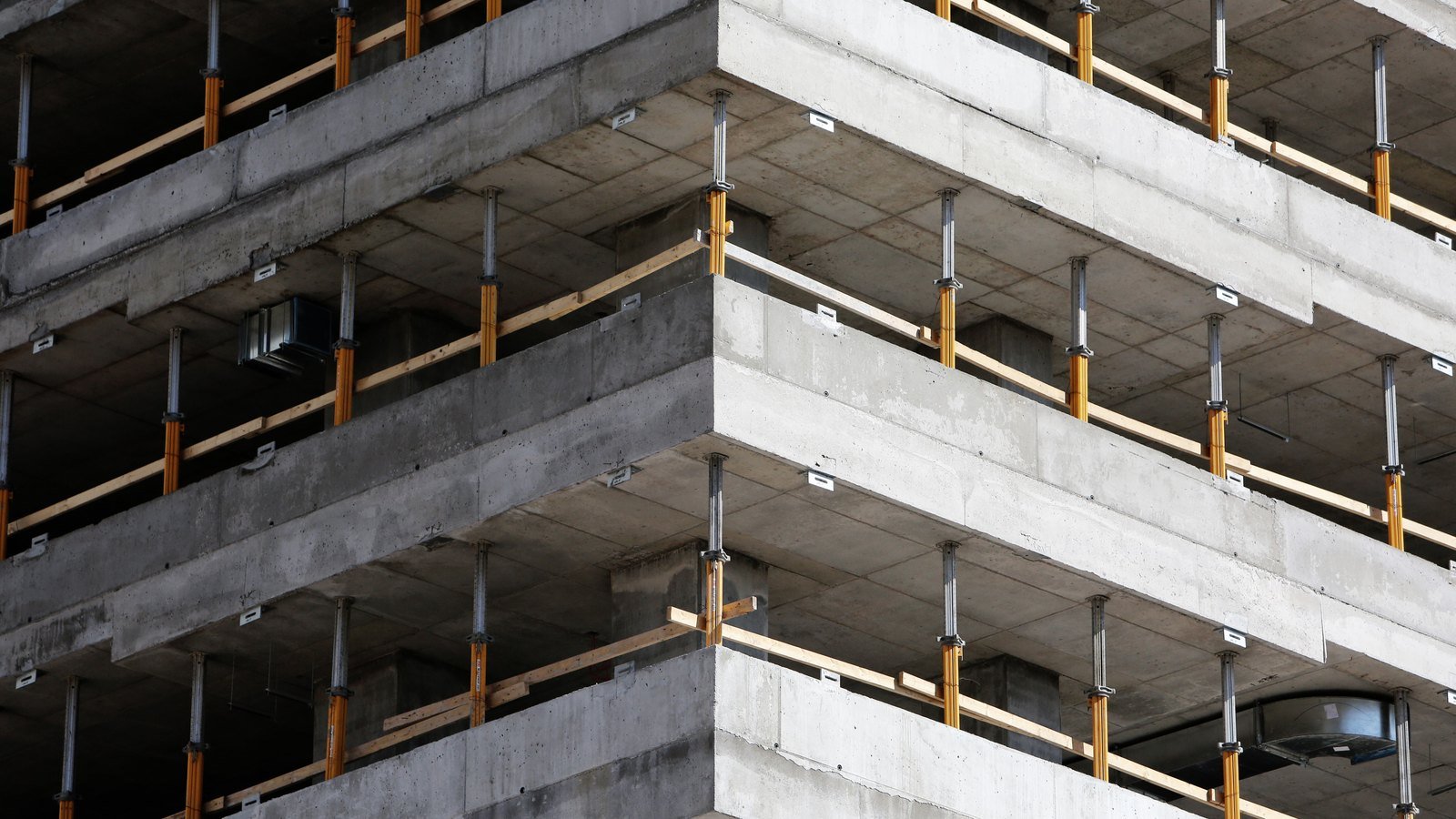The corner of a multi-storey concrete frame under construction with steel props and timber edge rails on each floor