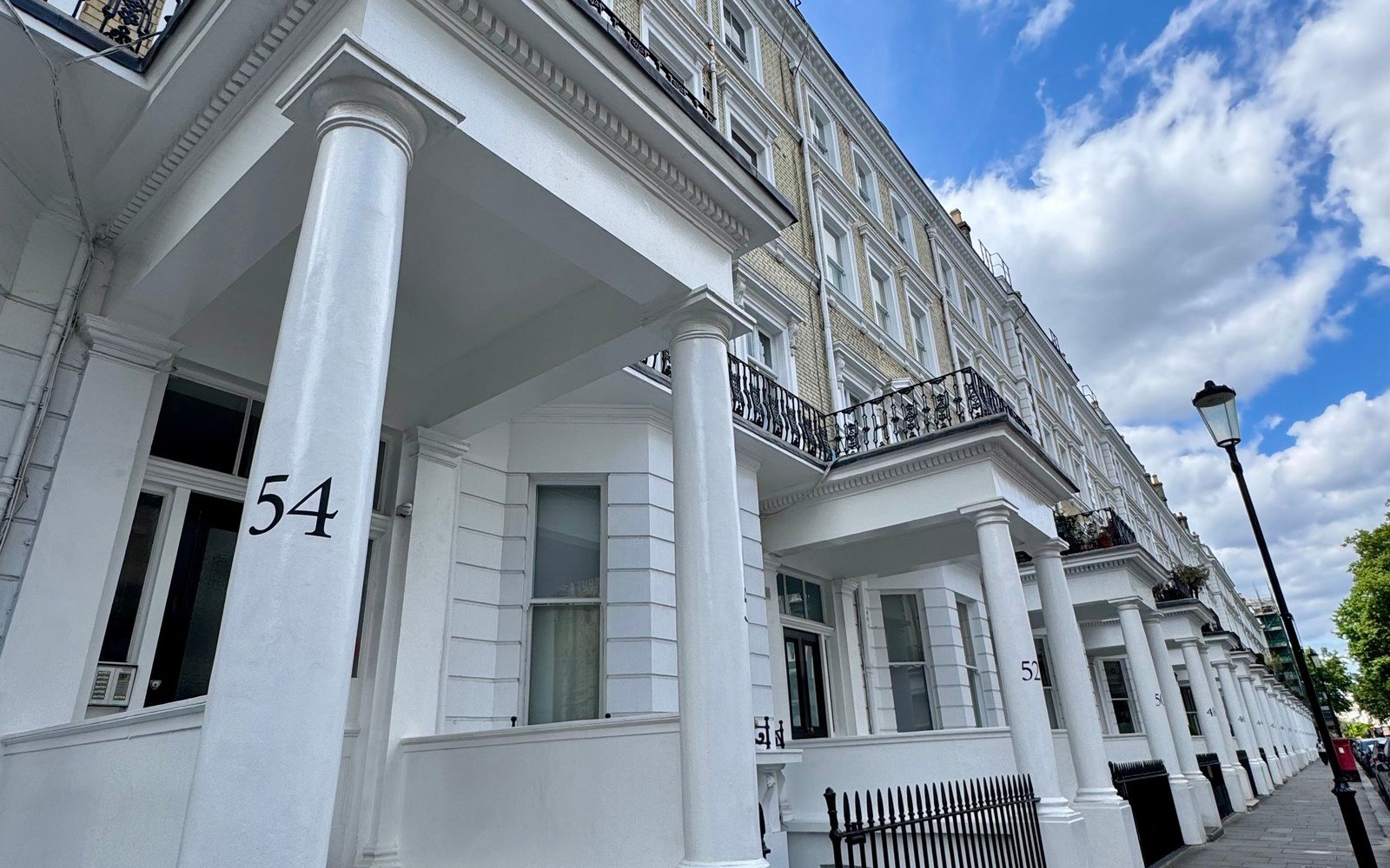 White stucco terraced houses with columned porticos and iron balconies along a London street under a blue sky