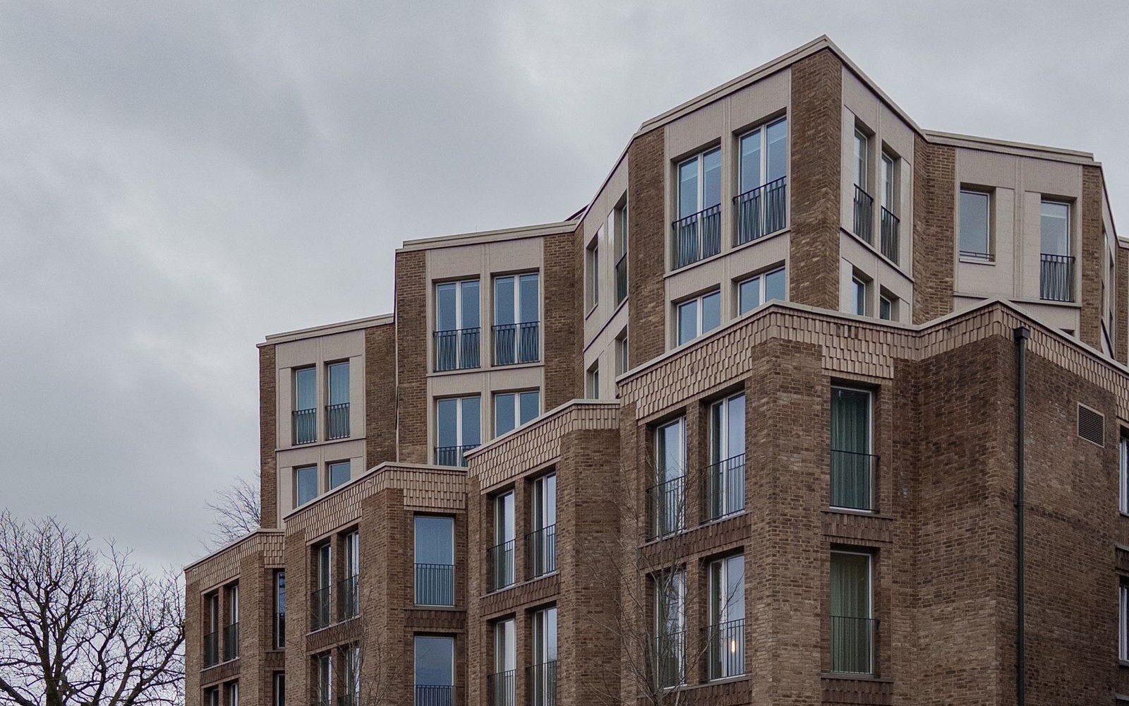 A modern brick apartment building of five storeys in north London, with recessed balconies and planting along the pavement wall