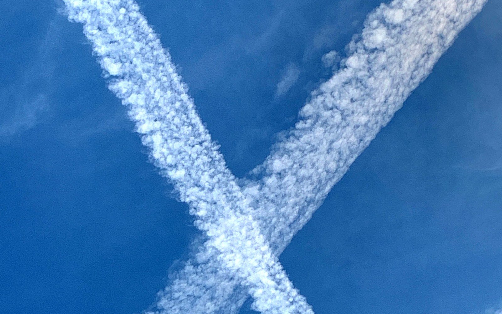 Two aircraft contrails crossing and spreading into thin cloud against a blue sky