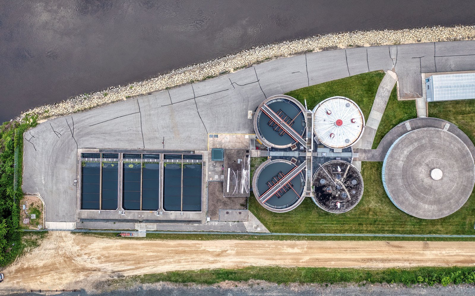 Circular settlement tanks and rectangular aeration basins of a water treatment works seen from directly overhead beside a river