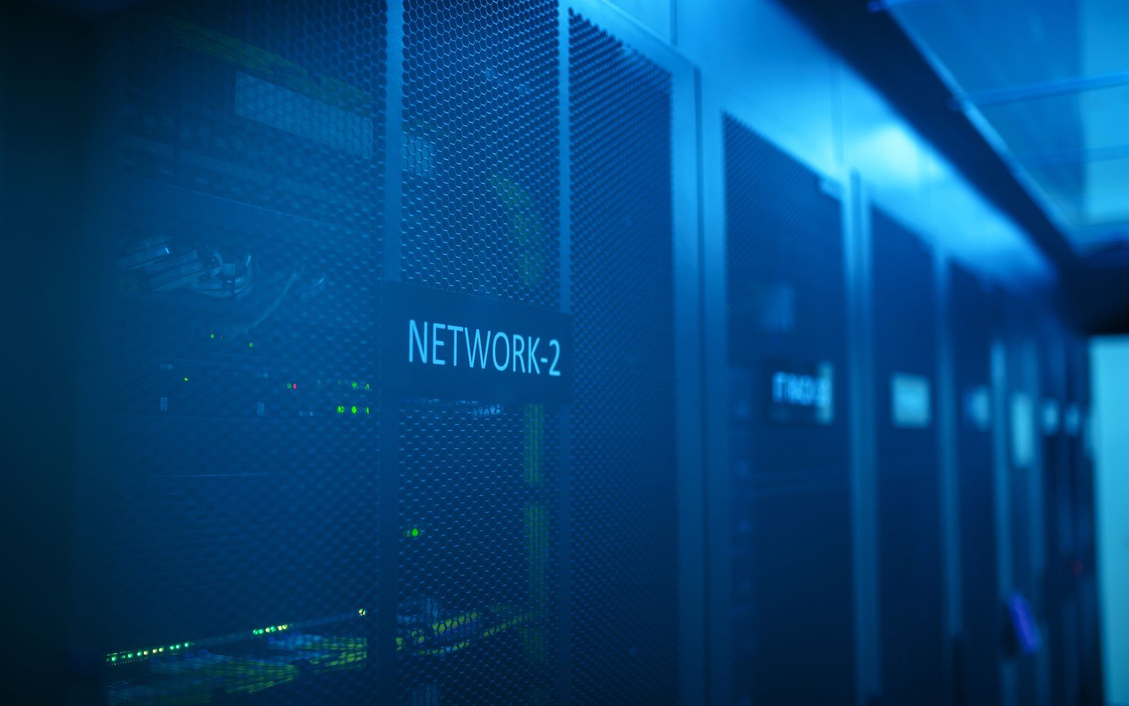A row of dark server cabinets under blue light in a data hall, one cabinet carrying a plain rack label