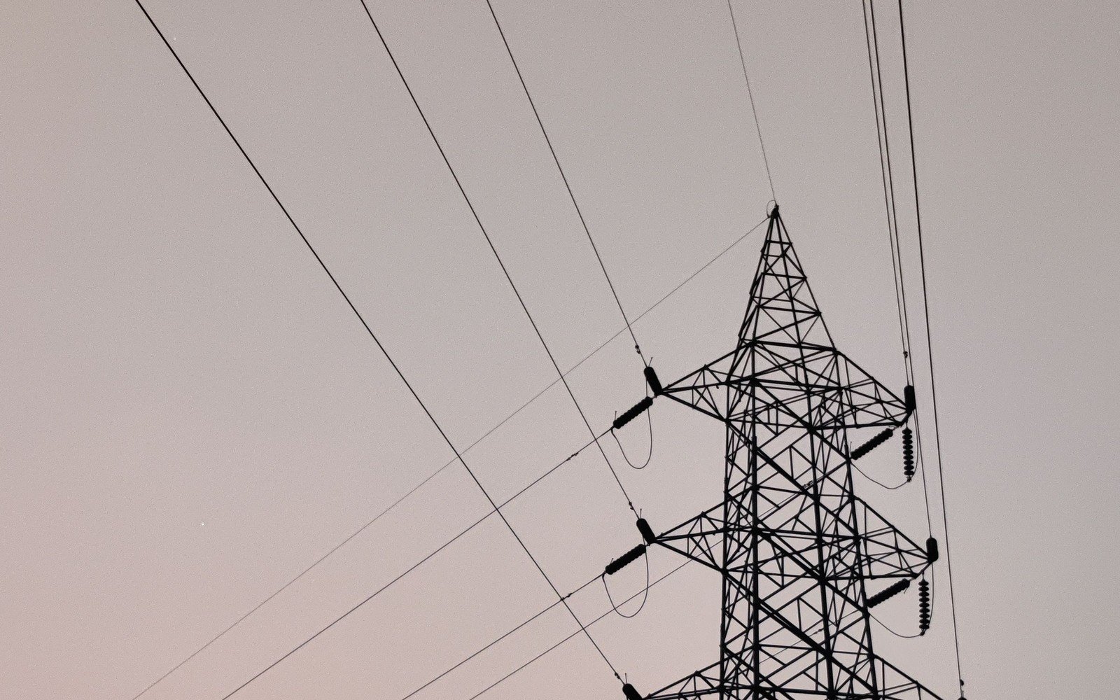 An electricity transmission tower and its overhead conductors silhouetted against a plain dusk sky