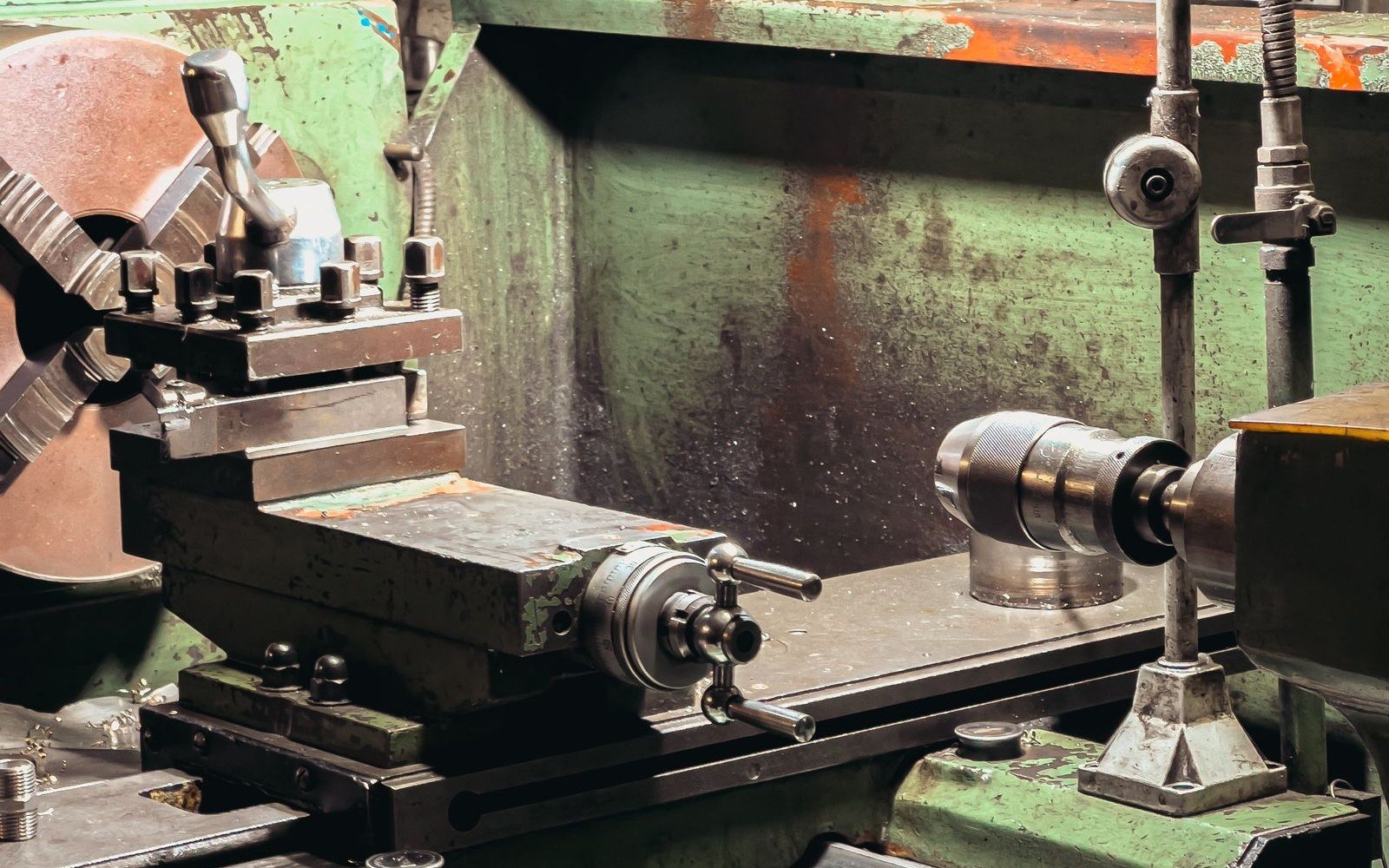 A green metal lathe in a workshop, with the tailstock and toolpost in the foreground and swarf on the bed