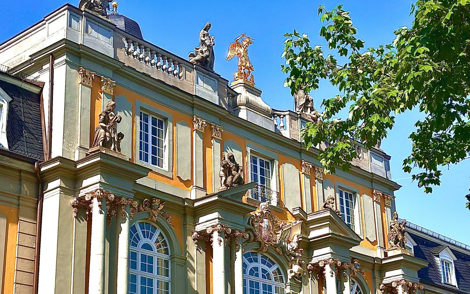 Baroque palace facade with rooftop statuary under a clear blue sky in Bonn, Germany