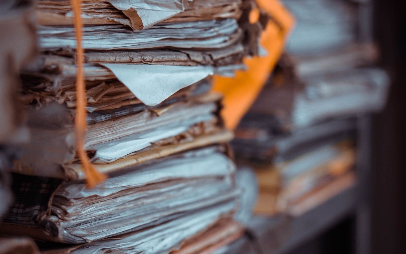 Stacks of tied paper files piled on a shelf, the topmost bundle in focus and the rest falling away