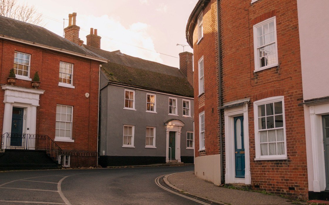 A curving street of brick and painted houses with white sash windows at first light