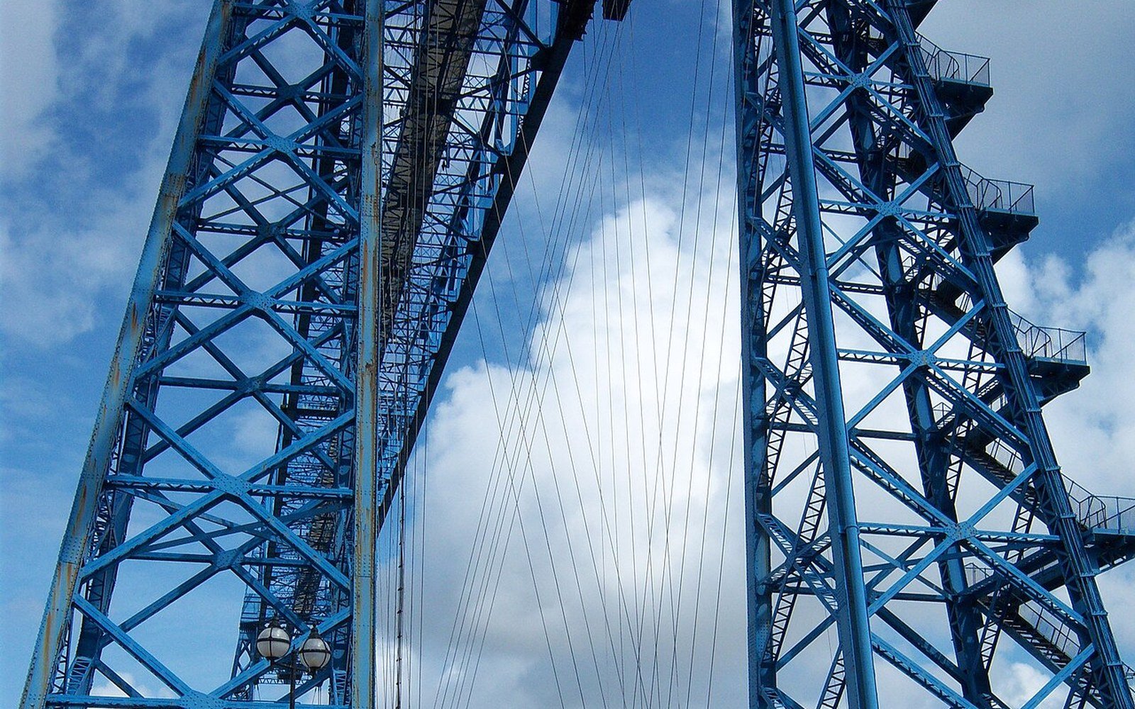The blue painted steel towers of a transporter bridge rising against a sky of broken cloud