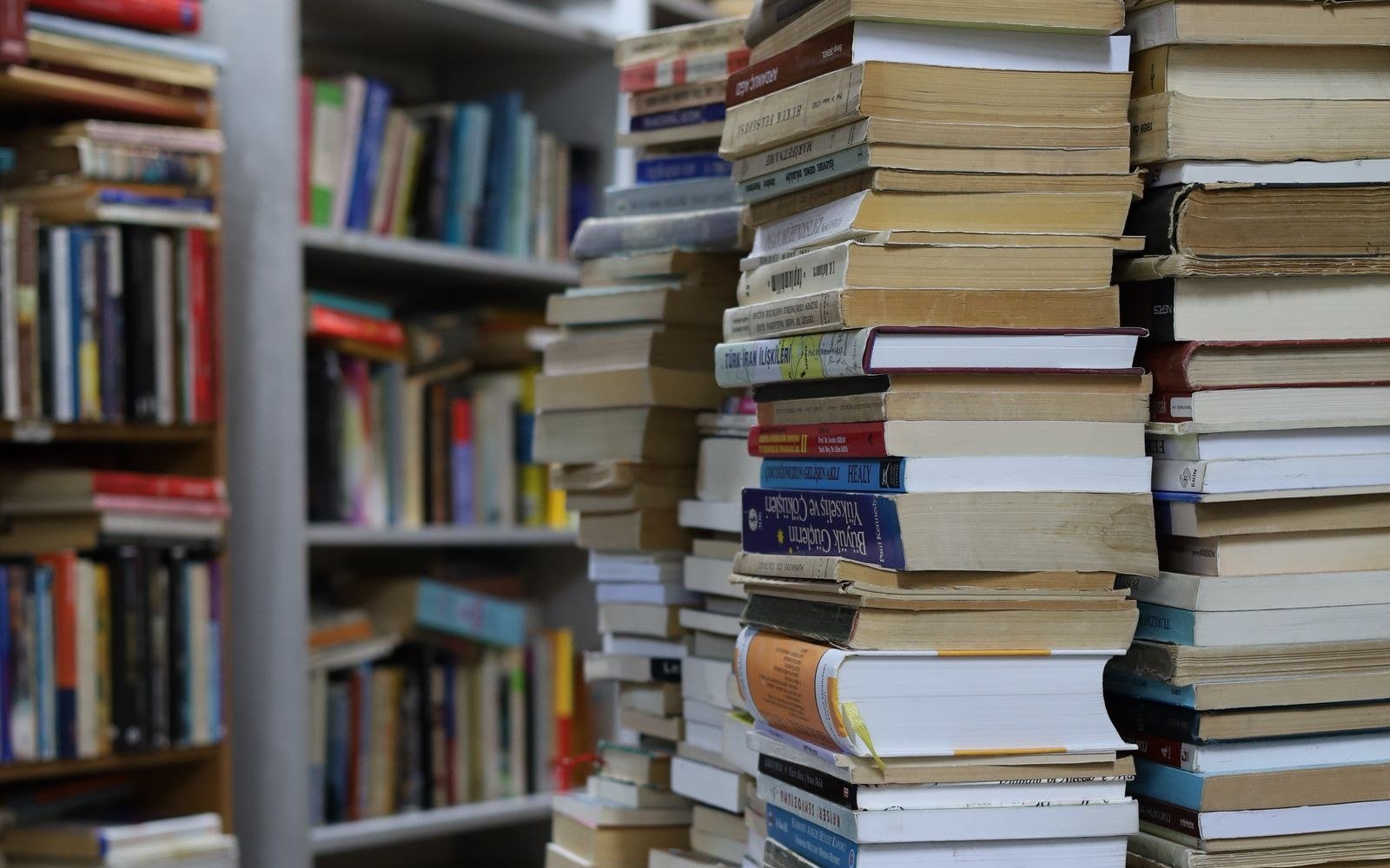 Stacked secondhand books piled beside a shelf of paperbacks in a bookshop