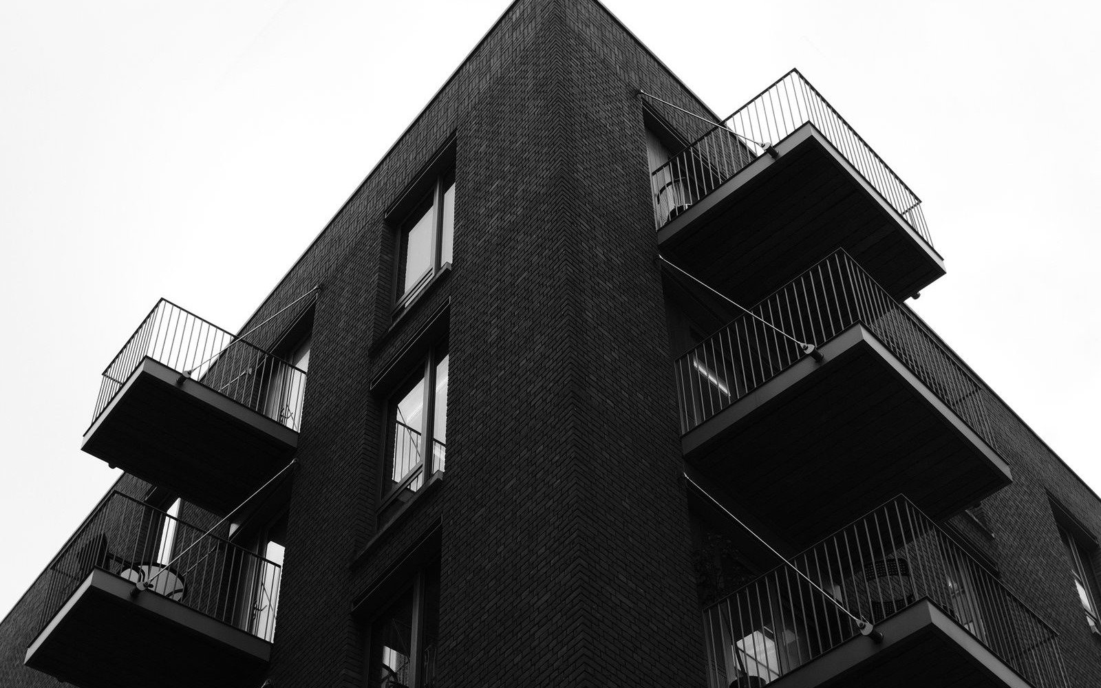 The corner of a dark brick residential block in London with projecting steel balconies, seen from below