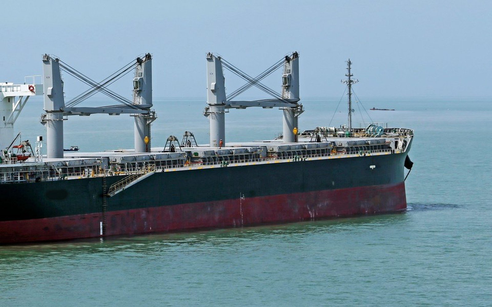 A geared bulk carrier with two pairs of deck cranes on a calm sea