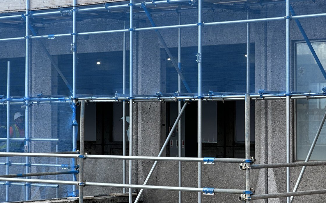 Blue scaffolding standing against a concrete building facade during refurbishment work