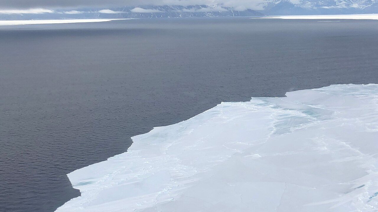 The edge of an Arctic ice sheet meeting open water, photographed from the air