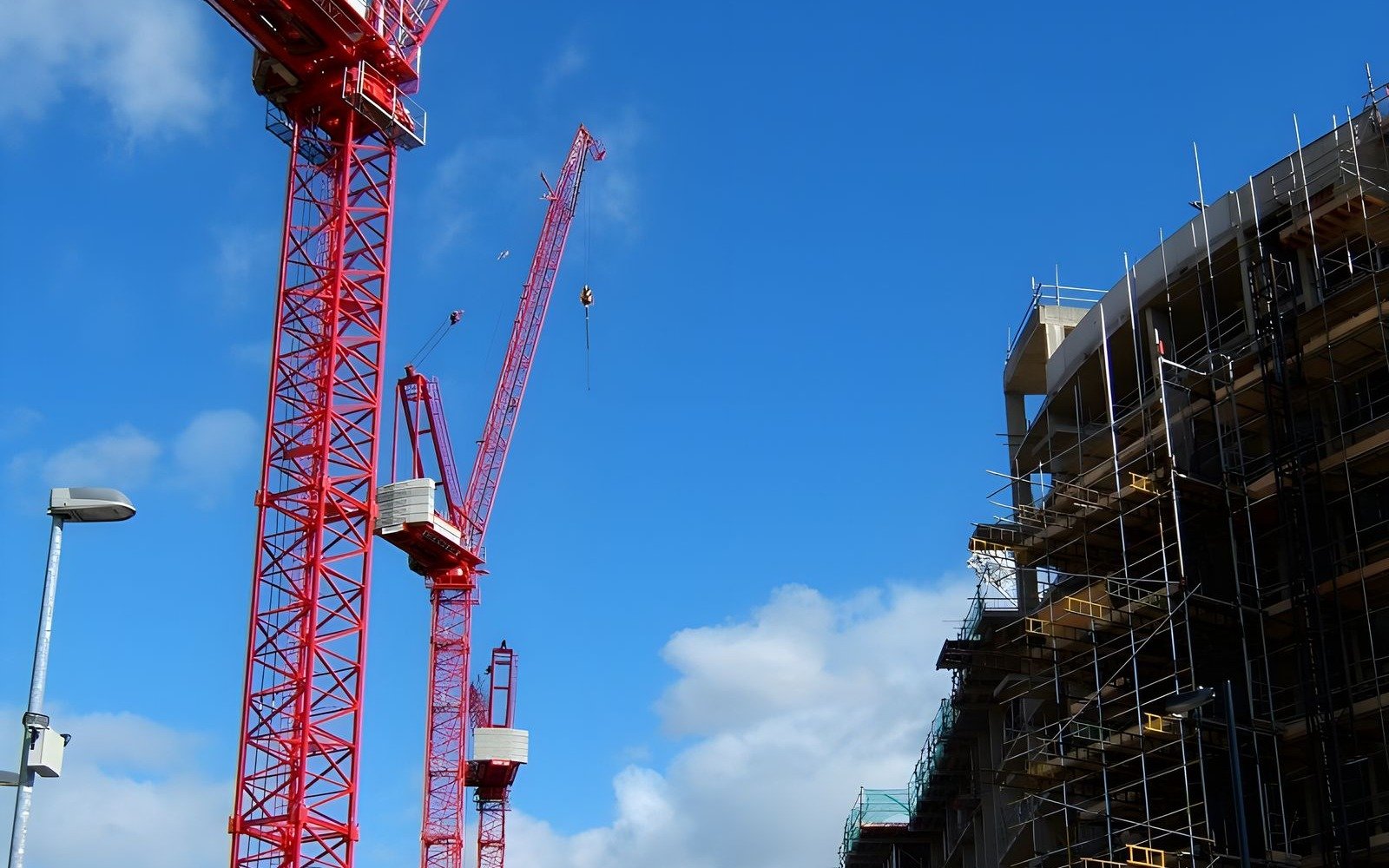 Two red tower cranes standing over a scaffolded building under a clear blue sky in London