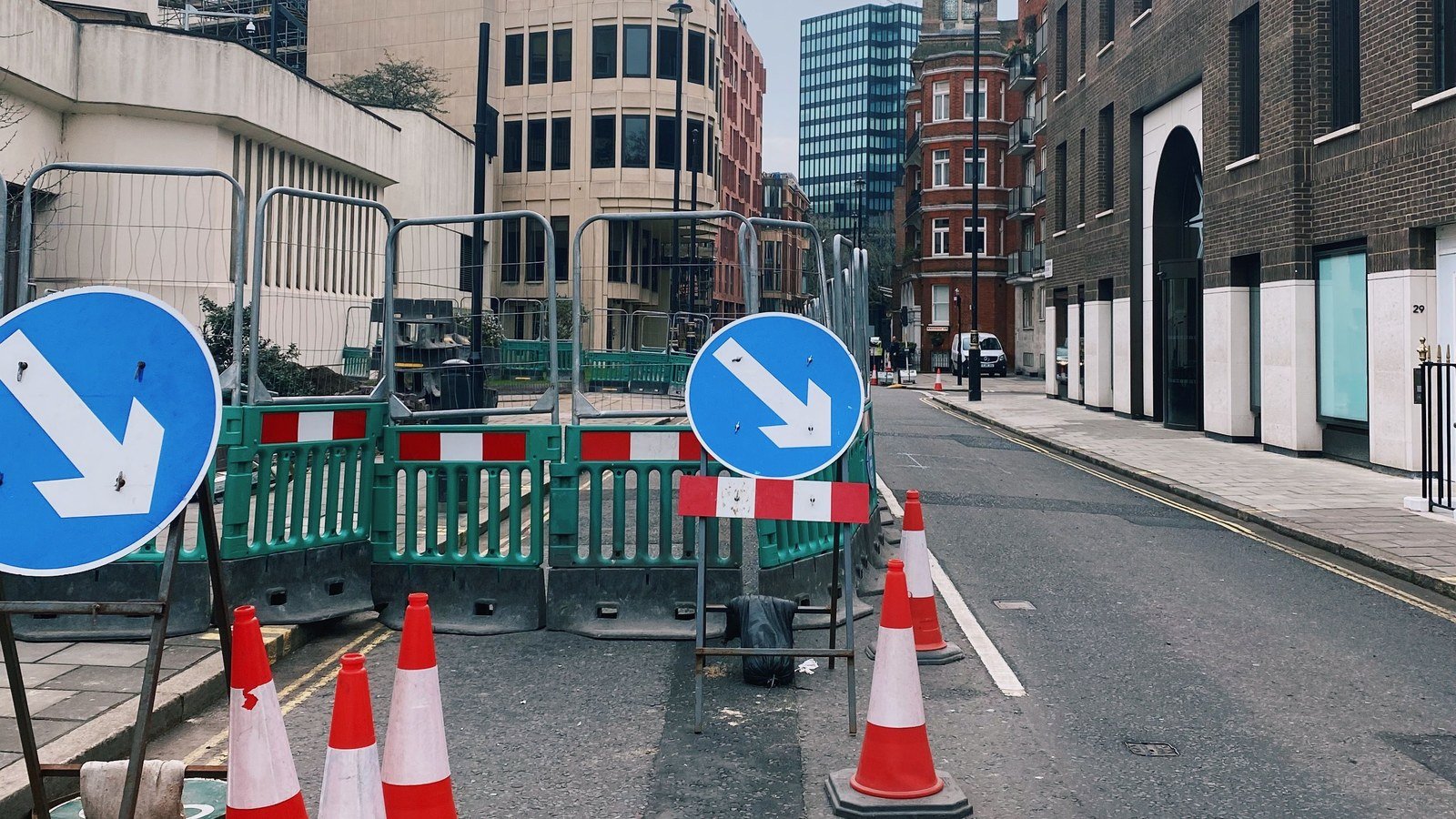Street works behind pedestrian barriers with keep left signs and traffic cones on a London street