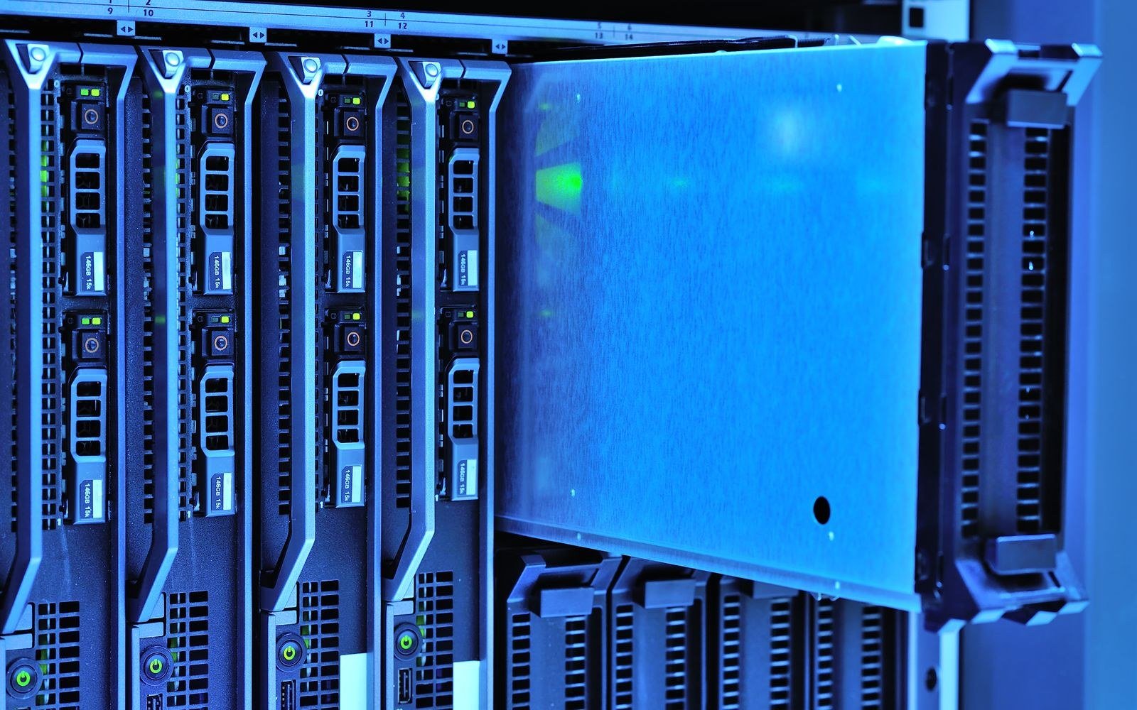 A close view of blade servers seated in a rack under blue light, one blade drawn part way out of its bay