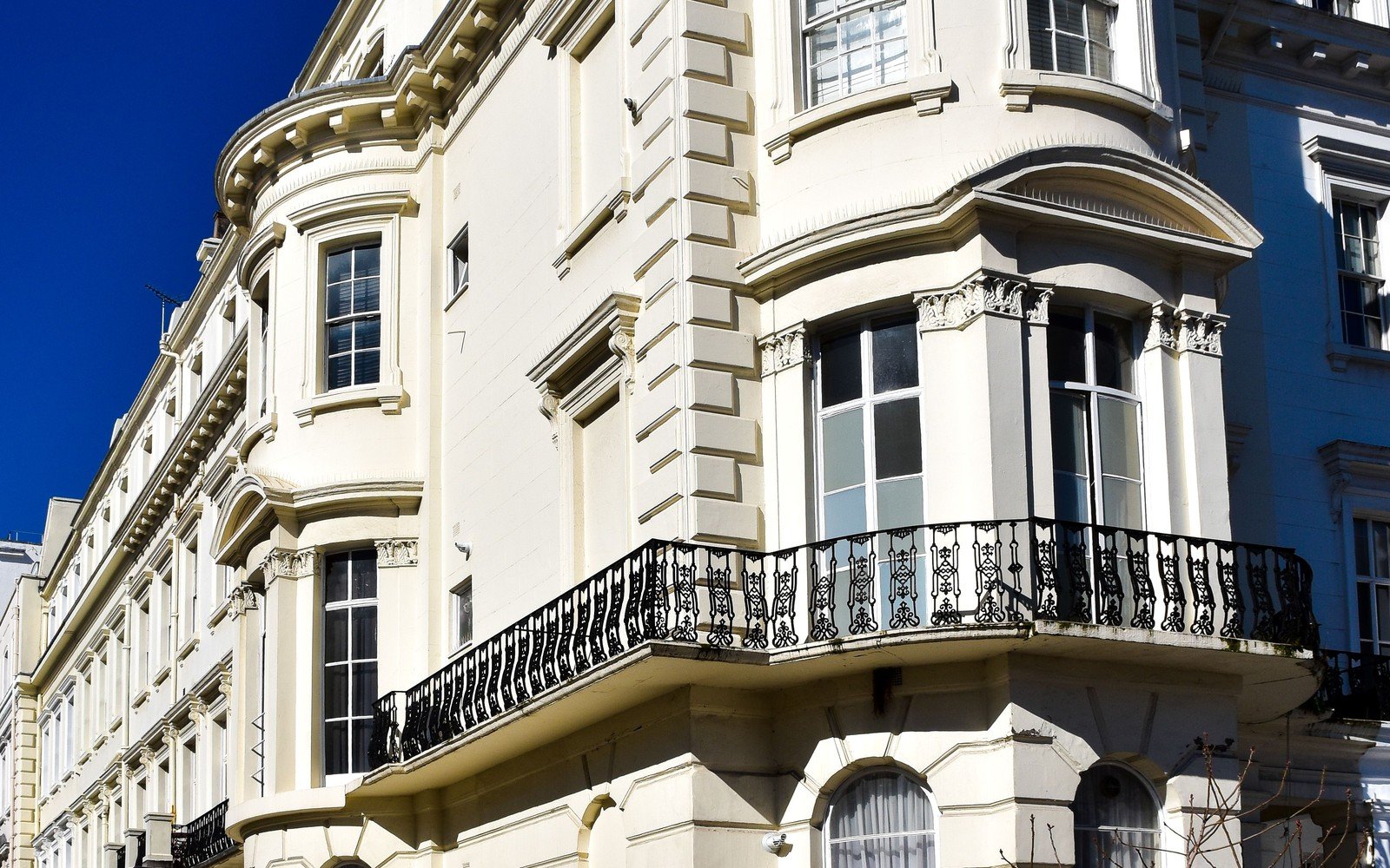 A cream stucco Victorian corner villa in London with a canted bay window and a long cast iron balcony, against a deep blue sky