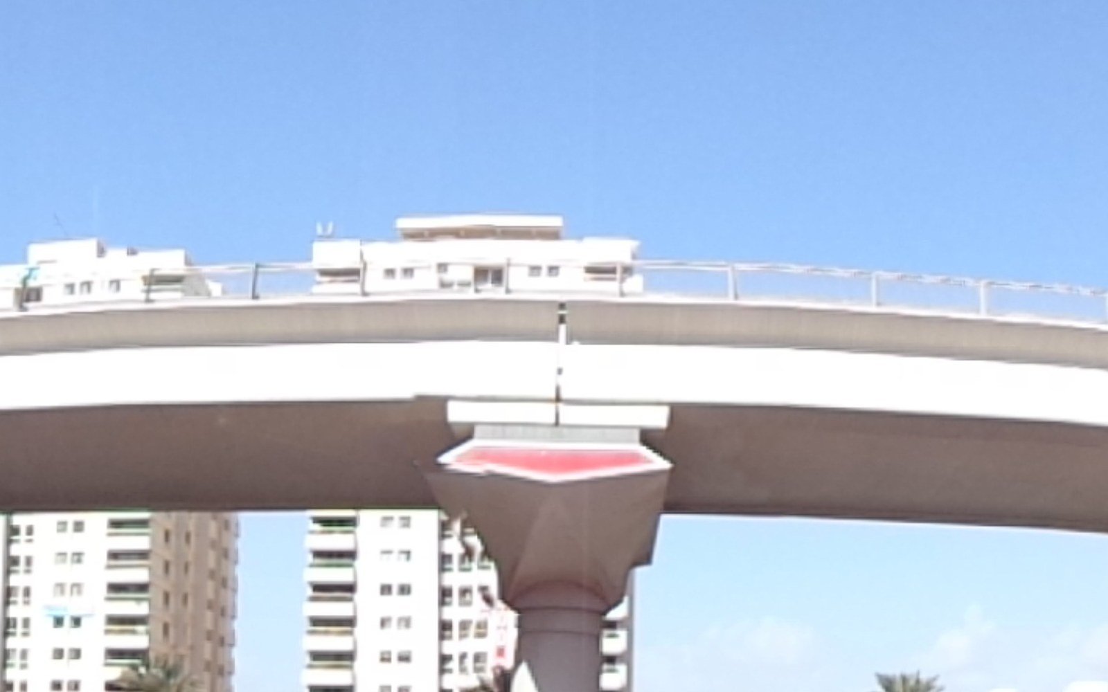 An elevated metro viaduct curves on tapered concrete piers between high rise residential towers under a clear sky