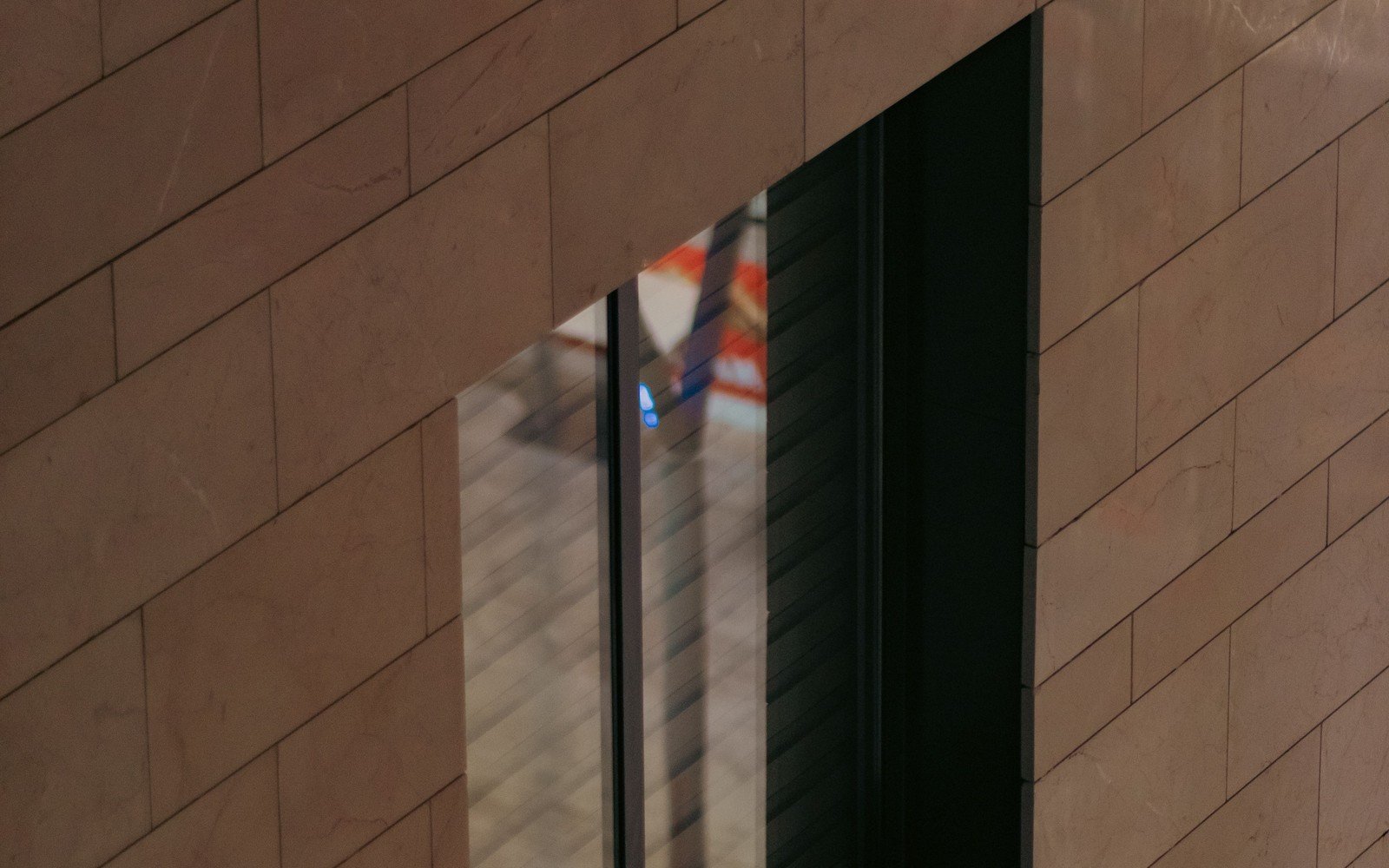 The stone-clad elevation of a modern office building, sand-coloured ashlar coursing running across the frame with a single deep window reveal, photographed obliquely with no signage on the wall