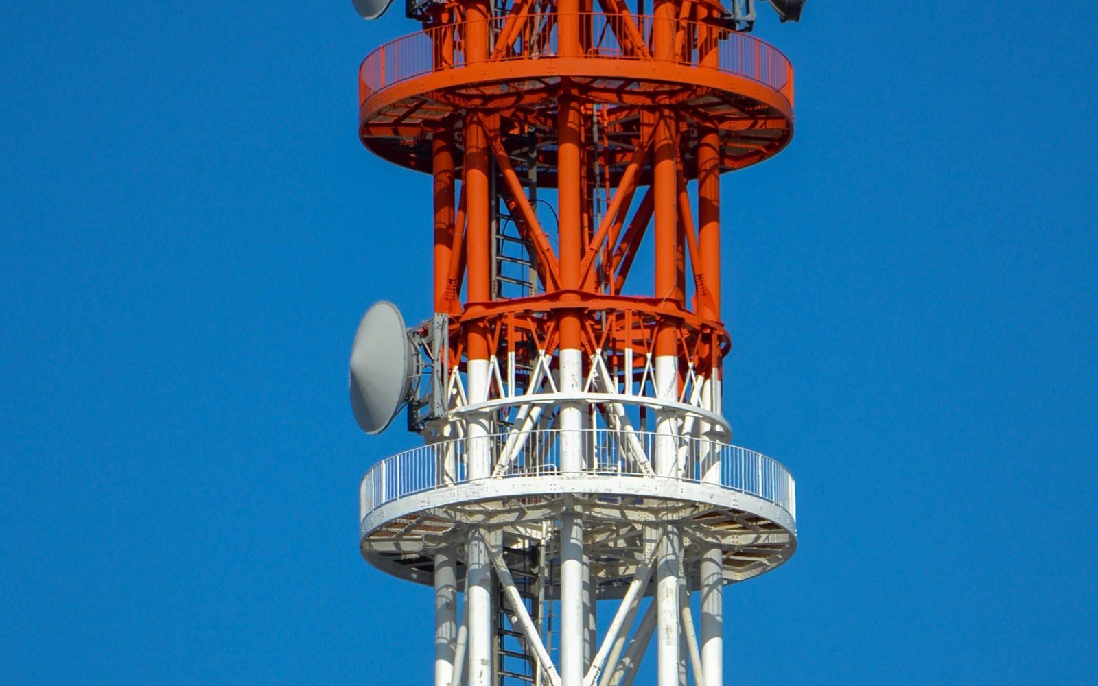Red and white telecommunications mast carrying antennas and dishes against a clear blue sky