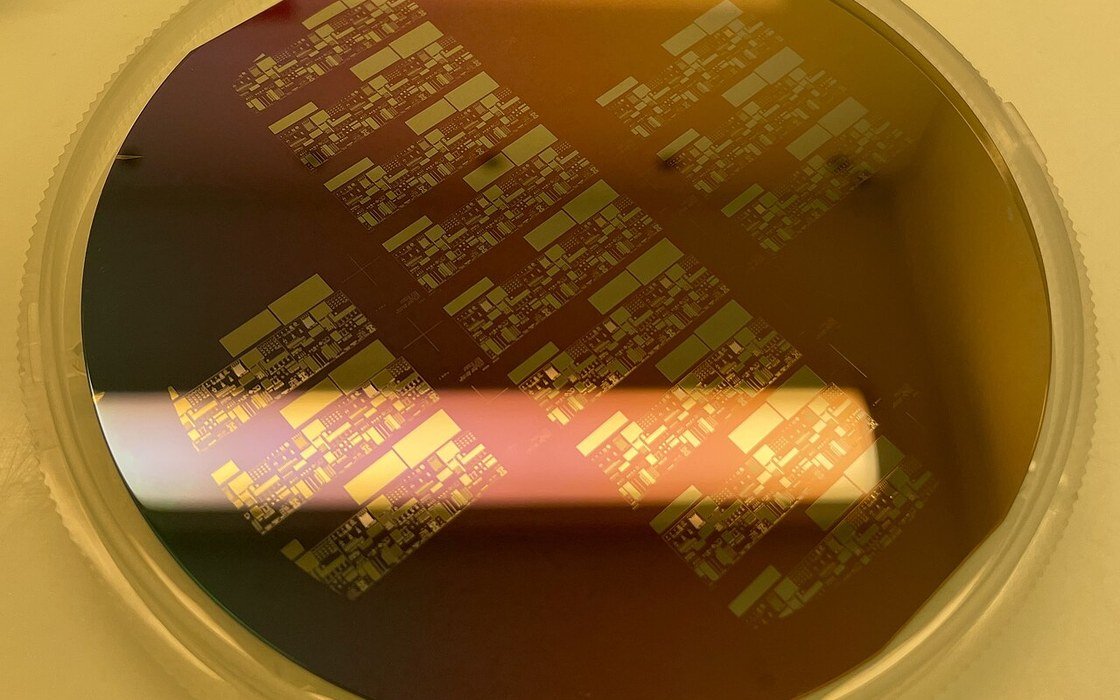 A single crystal silicon wafer under raking light, its oxidised surface showing bands of gold and rose colour and a pattern of etched rectangles