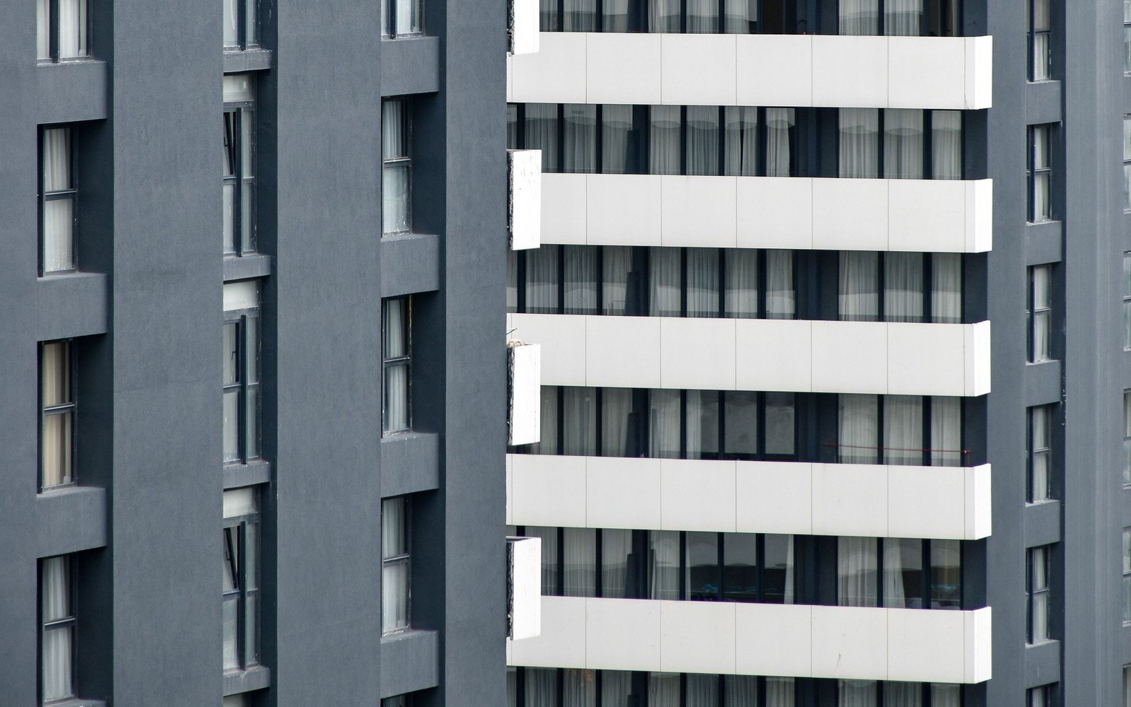 The banded facade of a completed high-rise residential block, white spandrel panels running across a smooth dark grey wall finish, with curtained glazing behind and no signage anywhere on the elevation