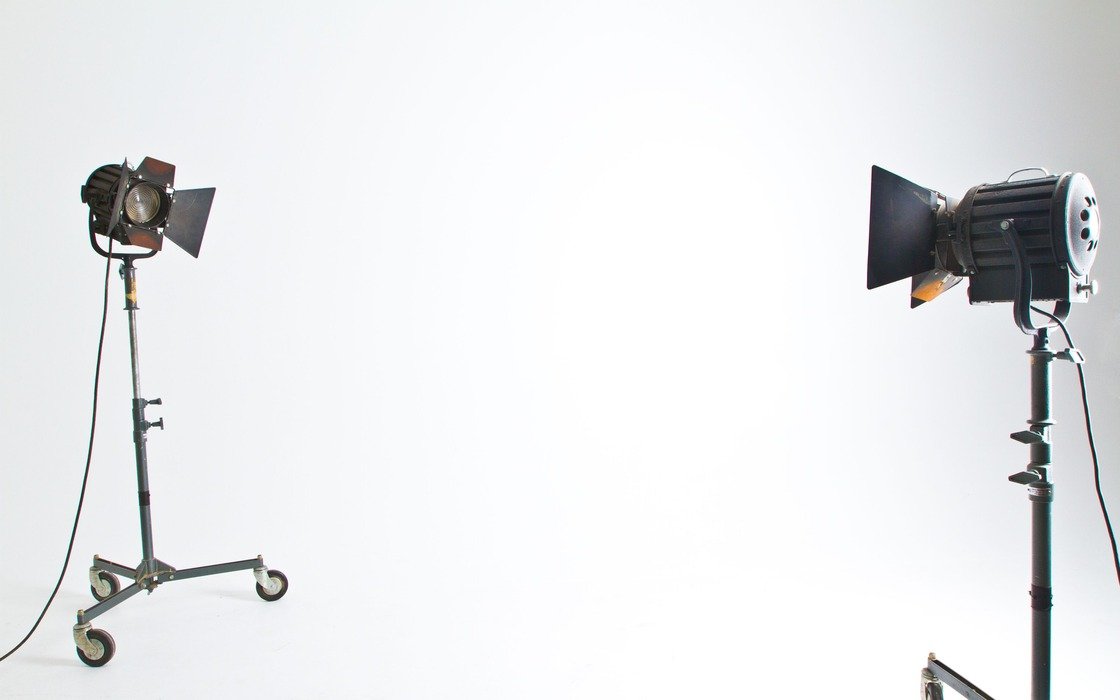 Two studio floodlights on wheeled stands facing each other across an empty white studio backdrop, barn doors open, cables trailing to the floor, location not identified