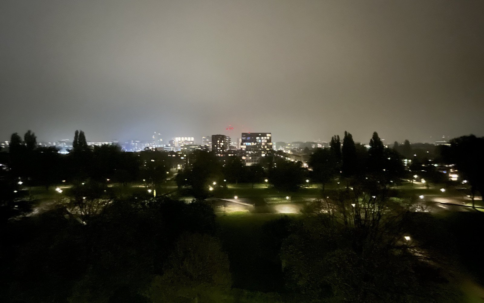 A distant view of the Amsterdam skyline at night, lit buildings low on the horizon under a dark sky