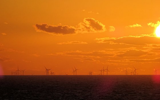 Offshore wind turbines silhouetted against the sunset over open sea