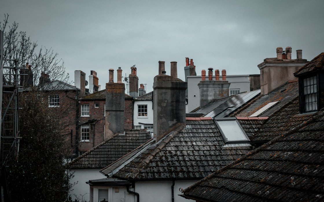 Tiled roof slopes, chimney stacks and rooflights across a group of older buildings under a grey sky