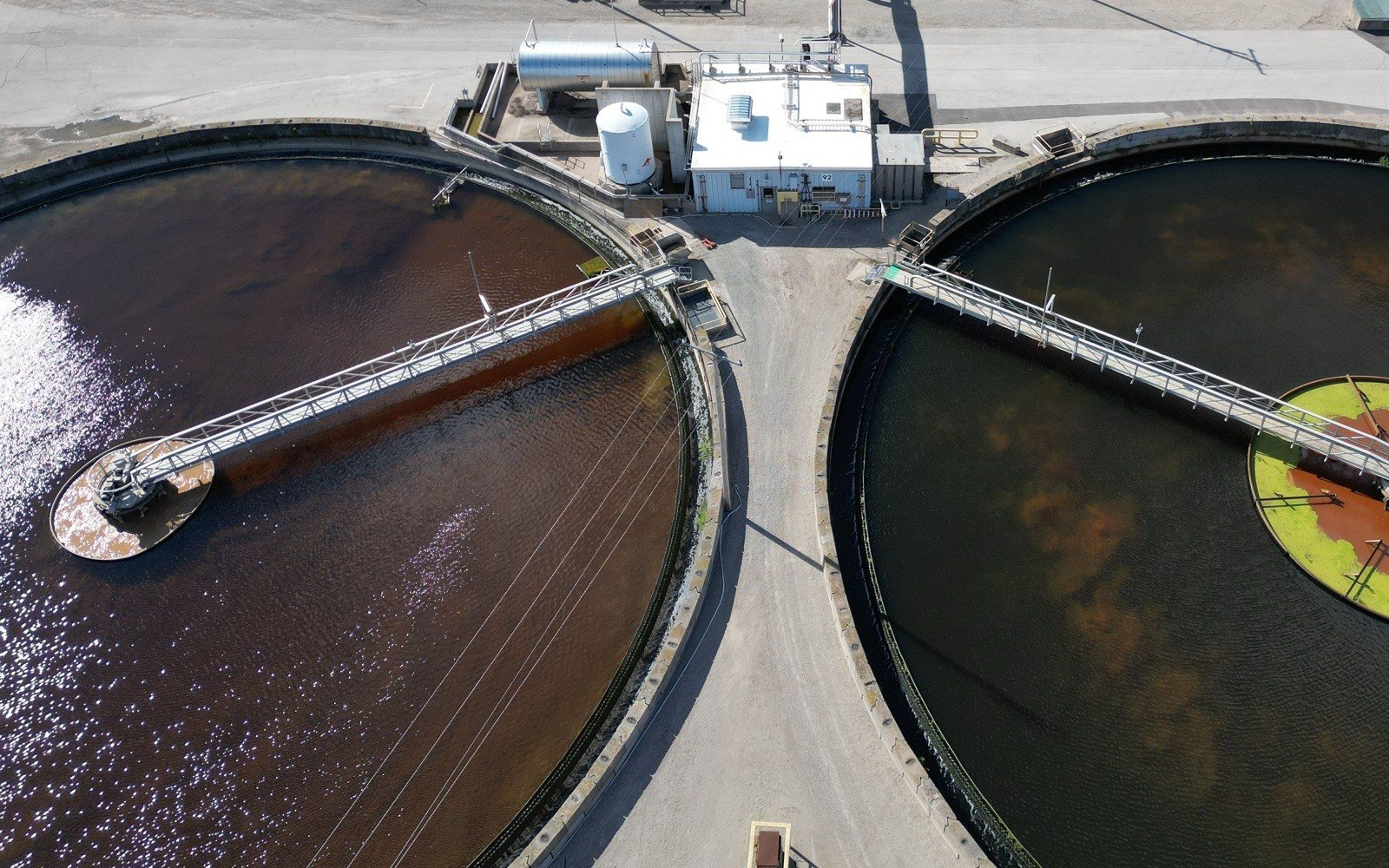 Two circular clarifier tanks with rotating bridge scrapers sit either side of a small plant building at a water treatment works