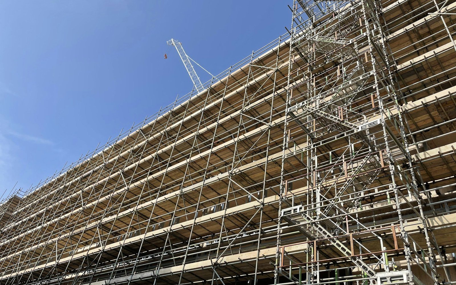 A large building fully clad in tube and fitting scaffolding with boarded lifts, ladders and a stair tower, photographed from below in Torquay, Devon