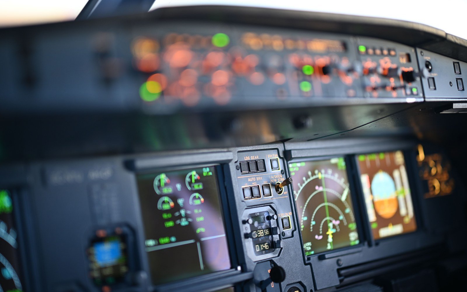 The forward instrument panel and overhead panel of an airliner flight deck at dusk, primary flight and navigation displays lit in the foreground and the overhead switch rows out of focus above