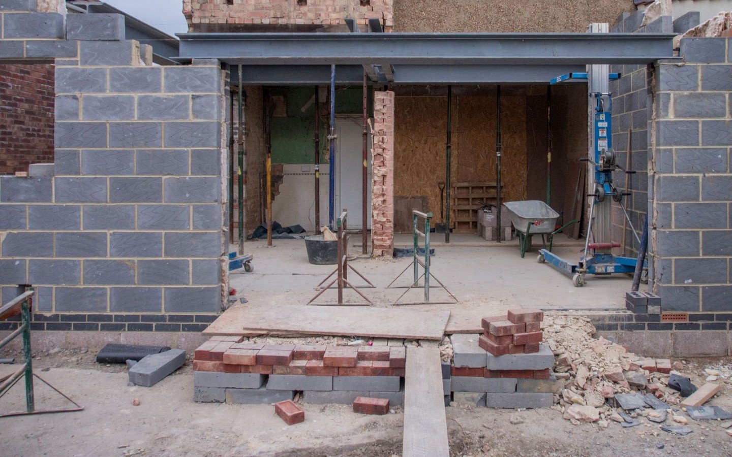 The blockwork shell of a rear house extension with a steel beam, adjustable props and stacked bricks