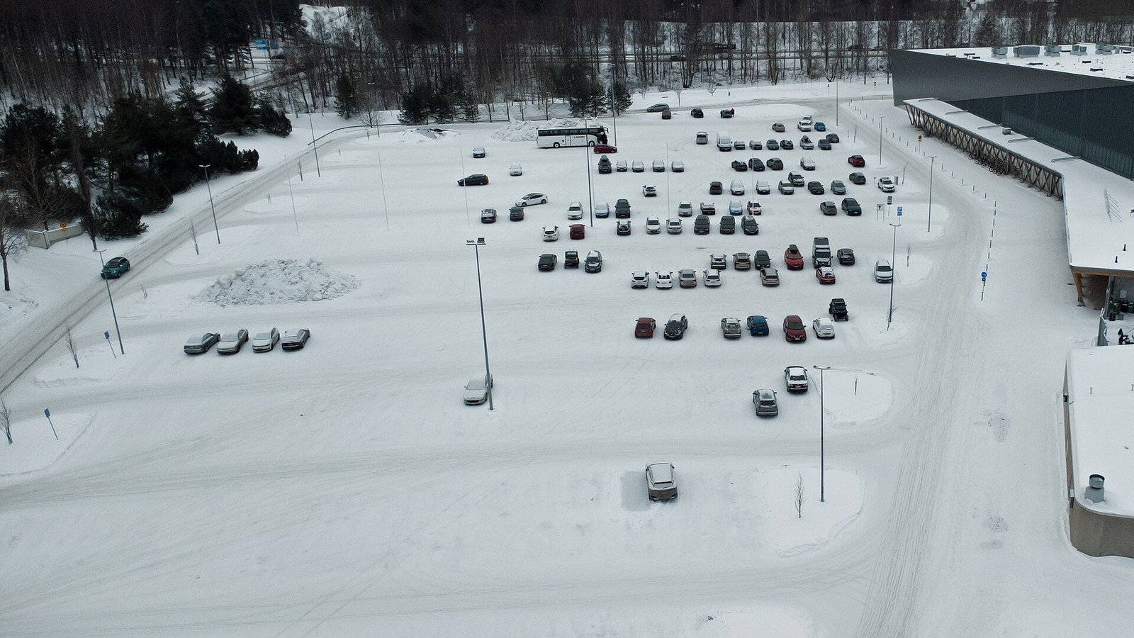 An aerial view of a snow-covered surface car park with vehicles standing in marked bays