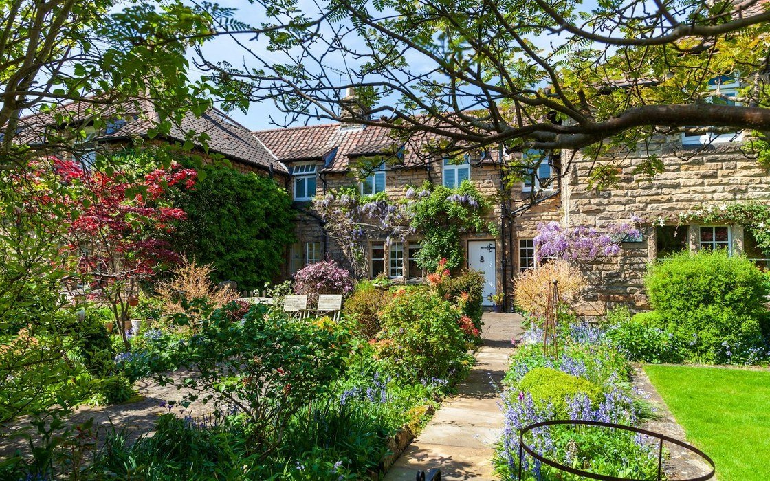 A terrace of old stone cottages behind a planted garden with a paved path leading to the door
