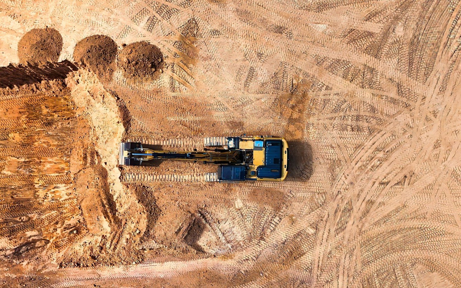 Plan view of a tracked excavator cutting into ground on a site criss-crossed with machine tracks