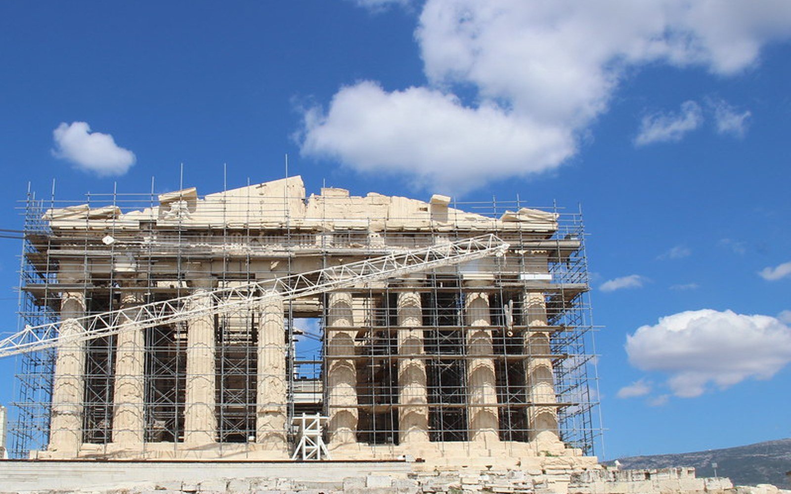The Parthenon on the Acropolis in Athens, wrapped in restoration scaffolding under a blue sky