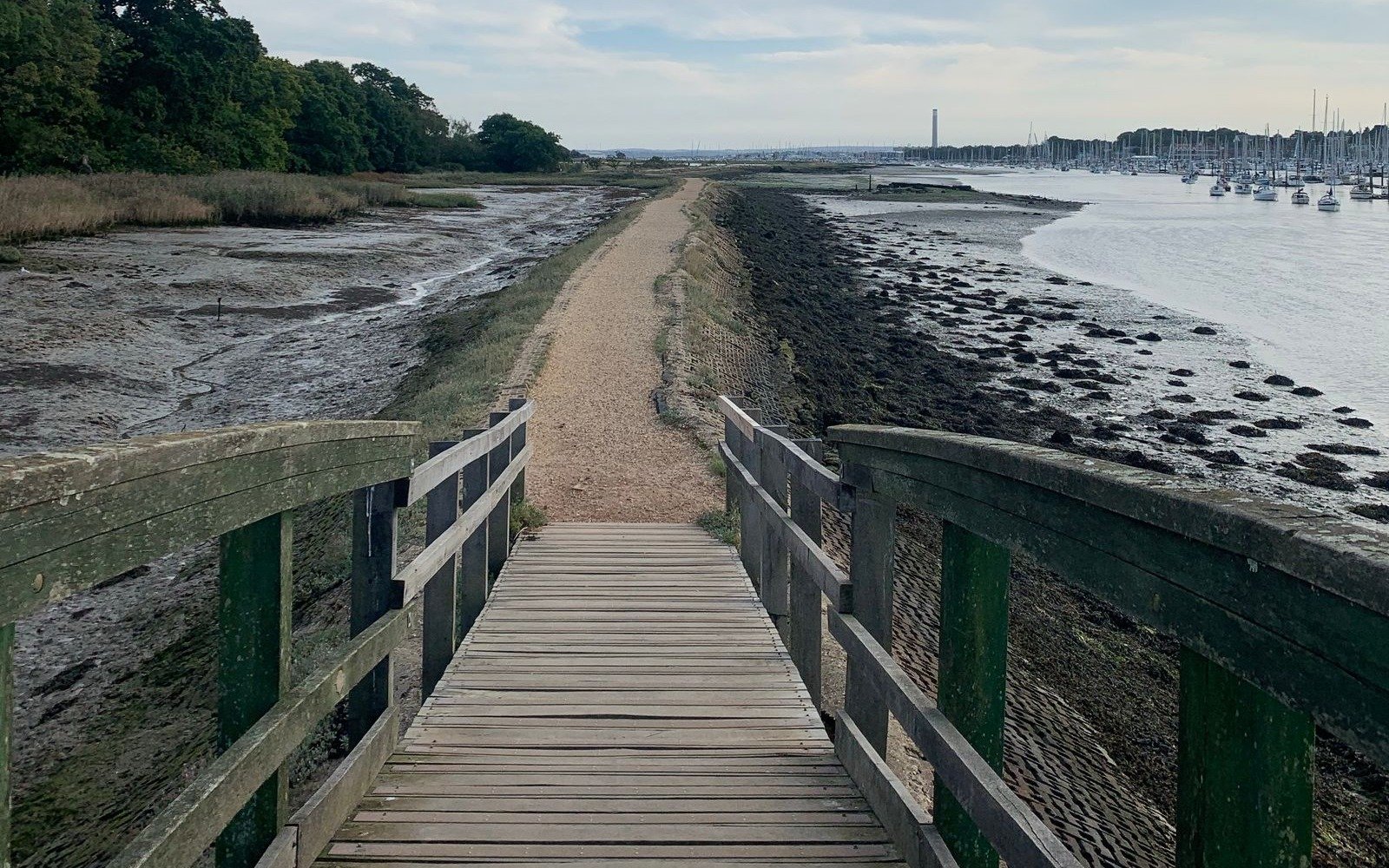 Wooden footbridge and shingle path between saltmarsh and moored yachts on the tidal shore near Southampton