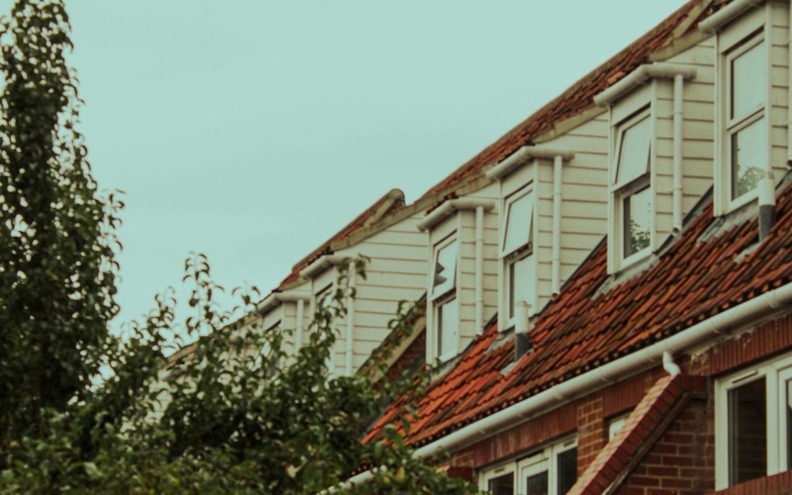 A terrace of English houses seen from below, showing clay tiled roofs, dormer windows, rendered upper storeys and red brickwork